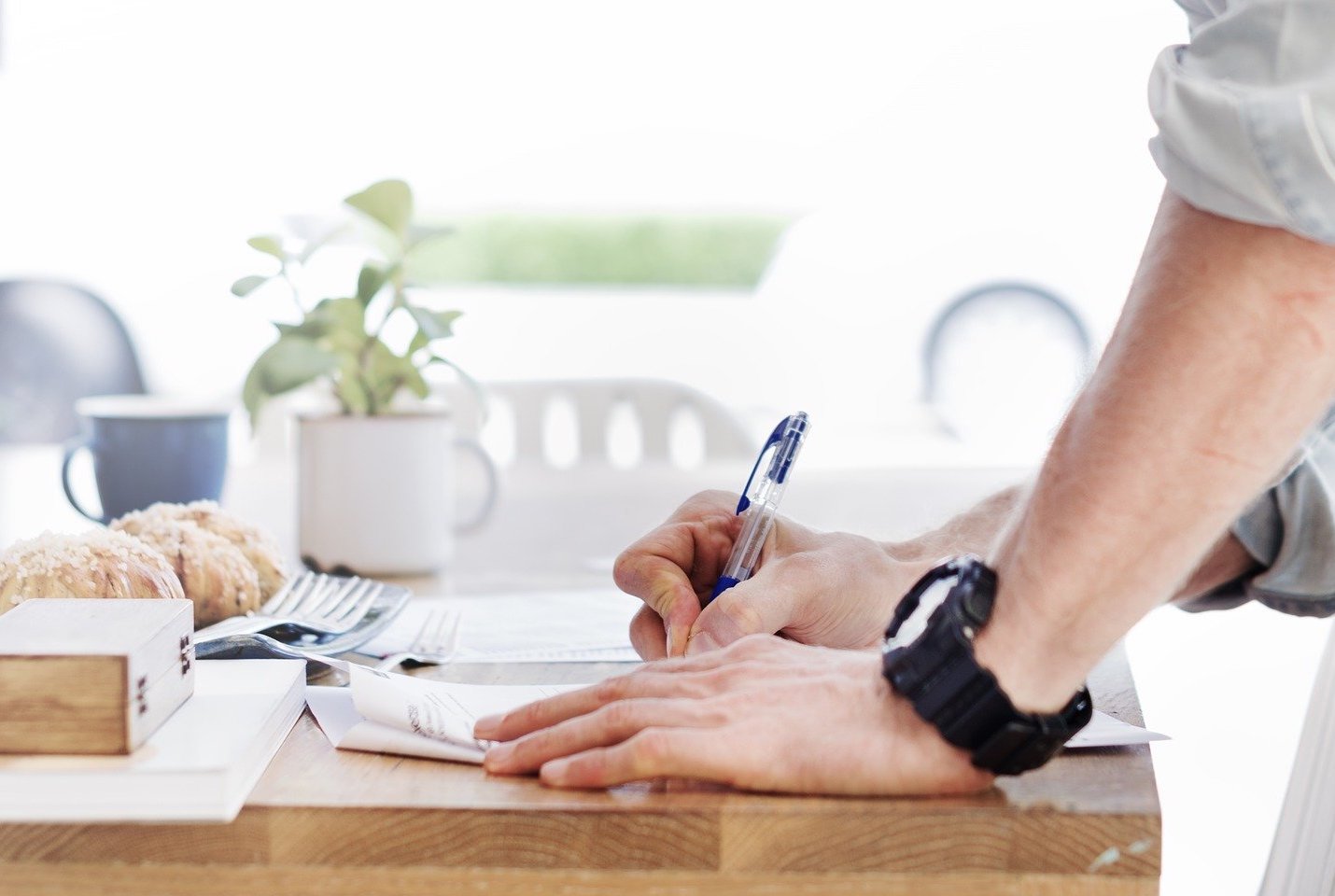 A home seller writes on a contract with a pen at their table.