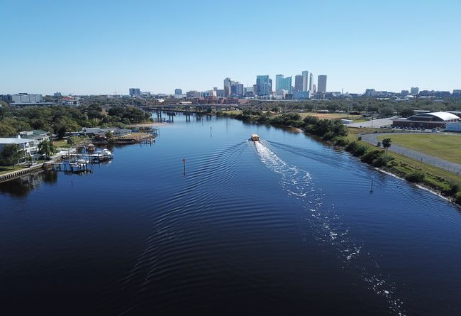 small boat in a large river with a downtown city in the background