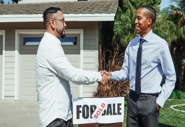 two men standing in front of a for sale sign closing a deal on a house | selling property with a lien