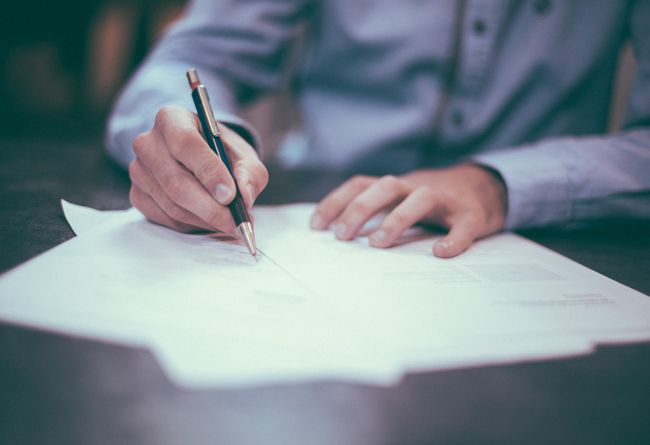 man sitting at a desk and writing on a piece of lined paper with a pen 