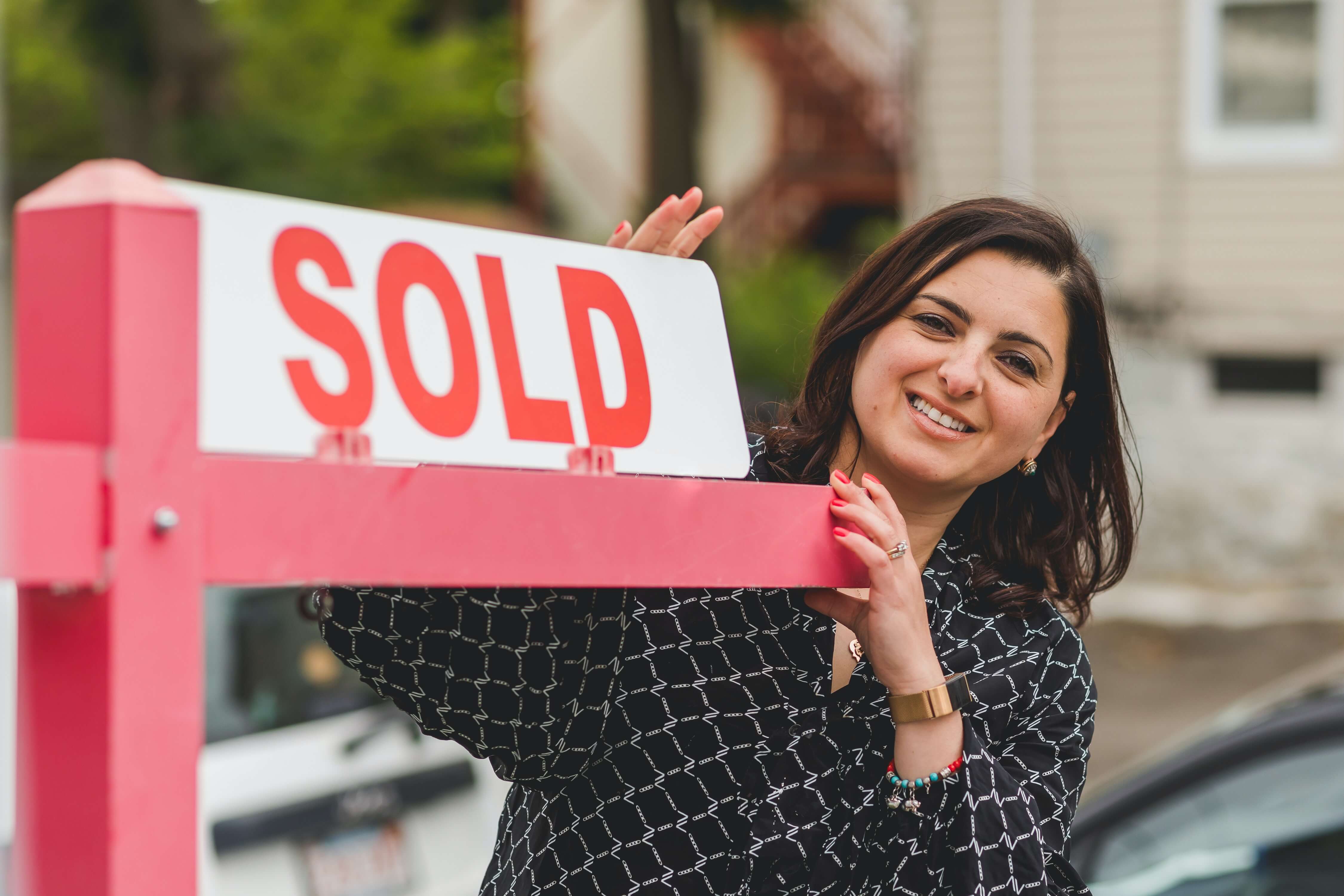 A woman stands with a sold sign next to her property that she sold with a lien on it.